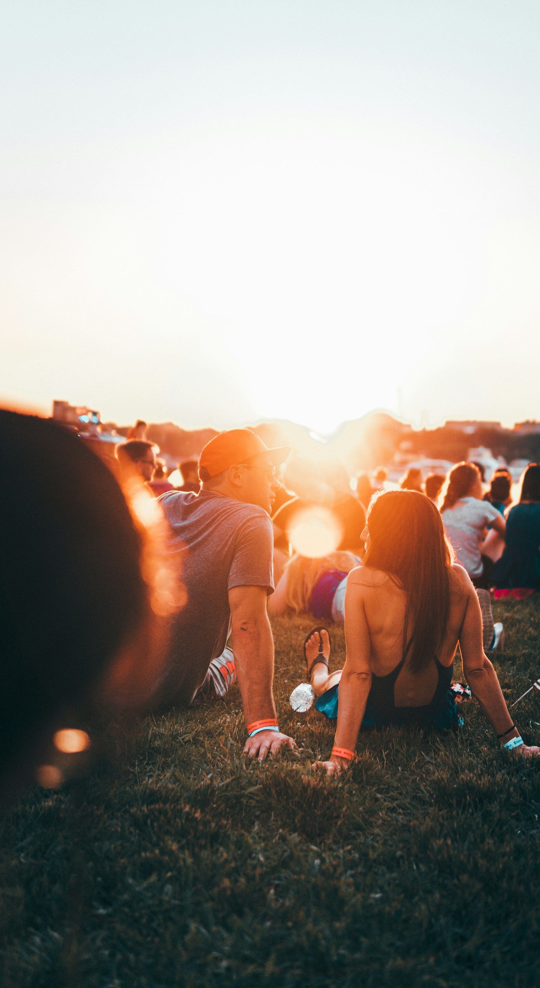 Le public d’un concert assis dans l’herbe face au soleil couchant